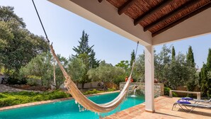 A pool area with a hammock, stone walls, and a tiled deck.
