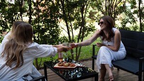 Deux personnes trinquent avec des verres de vin autour d’une table dont le plateau est noir, le tout étant entouré de verdure.