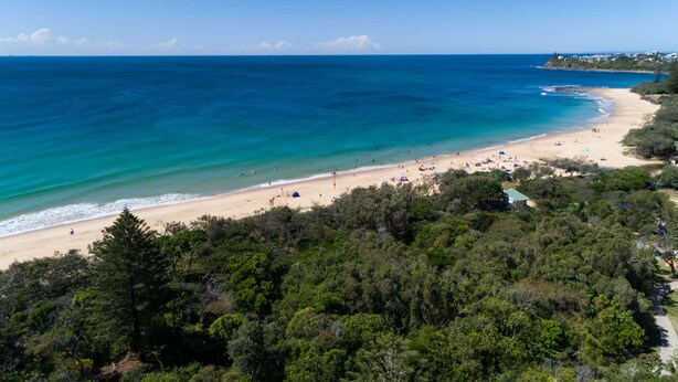 Une plage aux eaux turquoise et limpides, un rivage sablonneux et une végétation luxuriante et verdoyante au premier plan.