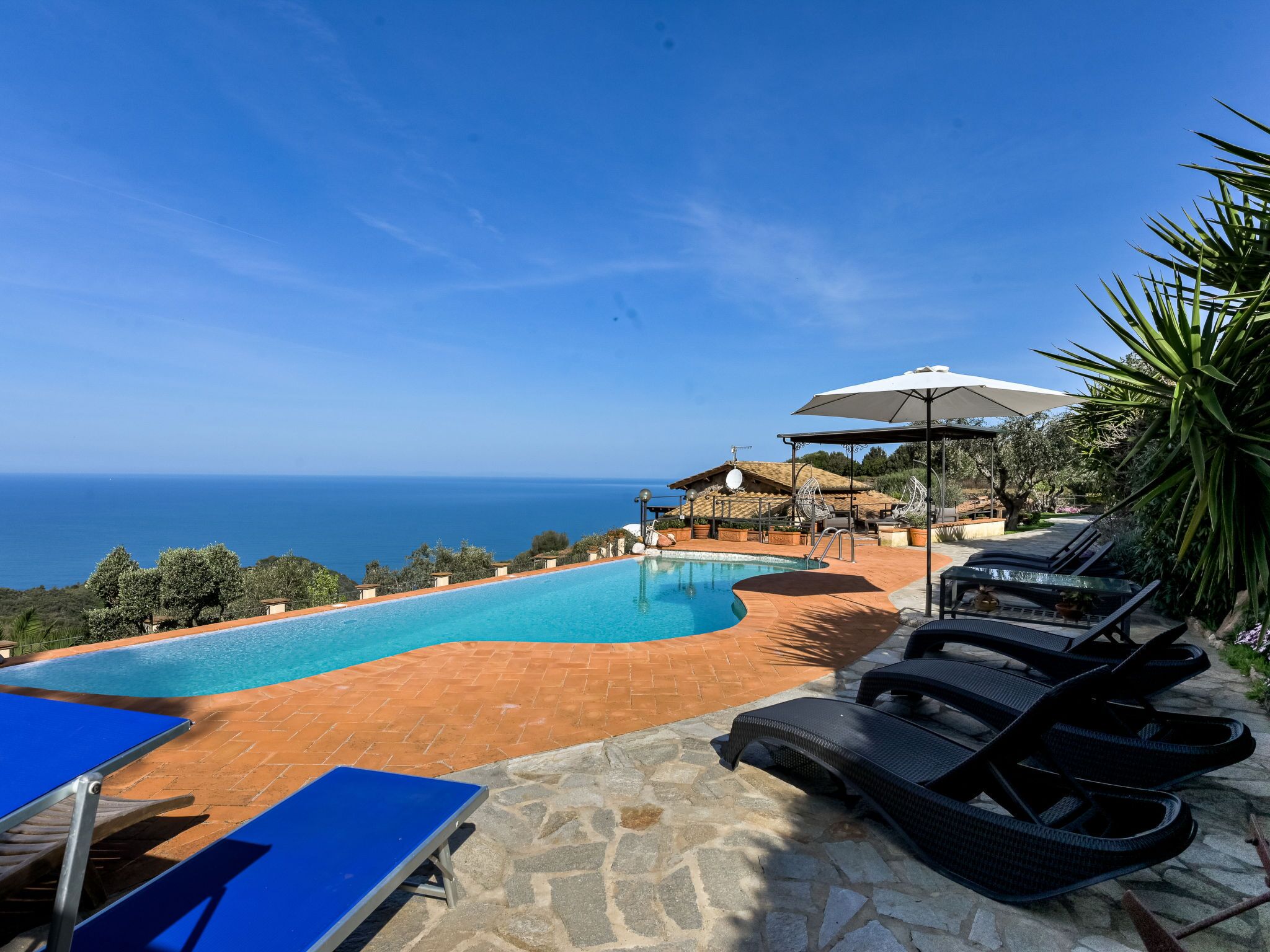 Un espace piscine avec vue sur la mer, des chaises longues et un coin salon abrité.