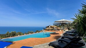 Zona de piscina con vistas al mar, sillas de descanso y un área de estar cubierta.
