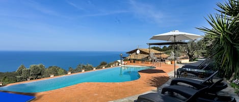 A pool area with a view of the sea, lounge chairs, and a covered seating area.