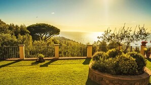 Un jardín bien cuidado con una maceta de piedra, una cerca metálica y vista al mar.