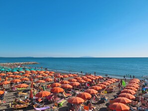 A beach with rows of orange umbrellas and beach chairs, a rocky shoreline, and the sea in the background.