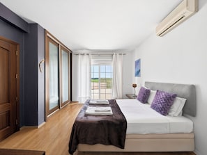 A bedroom with a bed, a nightstand, a window with curtains, and an air conditioning unit.