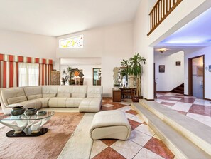 A spacious living area with a sectional sofa, a glass coffee table, and a large potted plant.