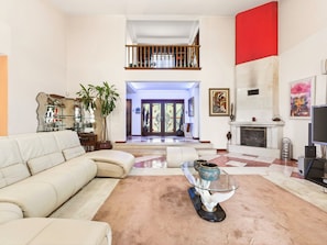 Amplia sala de estar con sofá, una mesa de centro de vidrio, chimenea y escalera que conduce a un nivel superior.