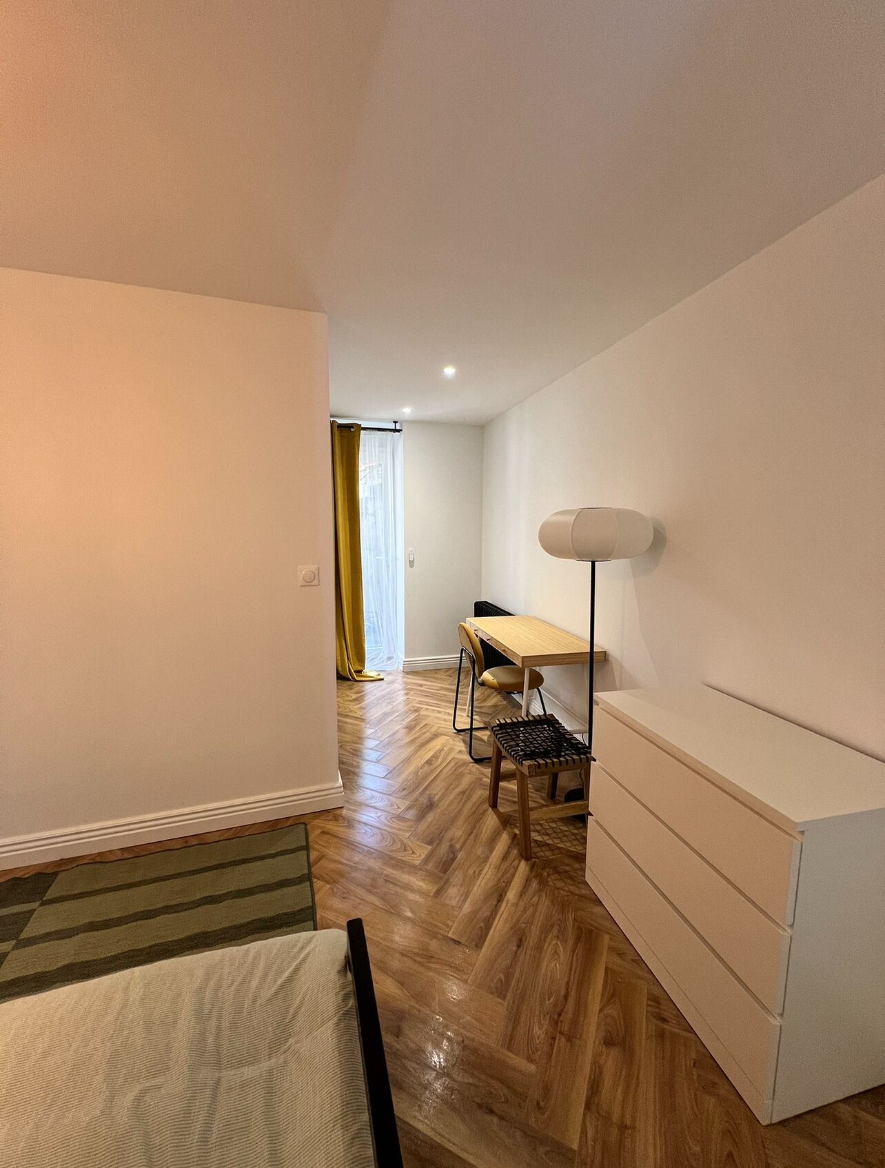 A room with a bed, a desk, a chair, and a lamp.