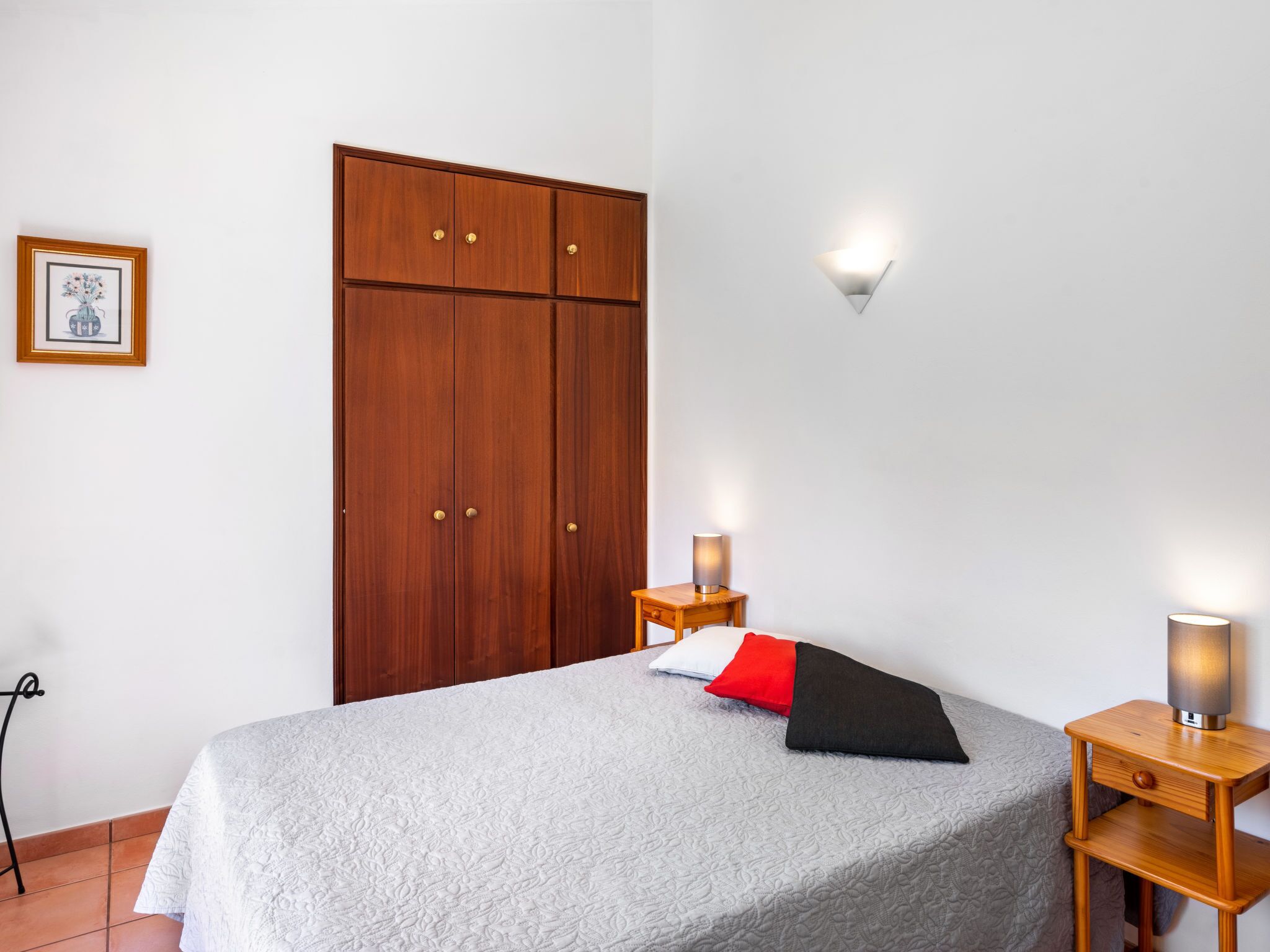 Une chambre à coucher comprenant un lit, une armoire, une table de chevet, une lampe fixée au mur et un tableau encadré accroché au mur.