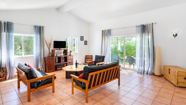 A spacious living room with wooden furniture, a television, and a large window with curtains.