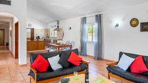 A living room with a sofa and a coffee table, a kitchen in the background, and a dining area.