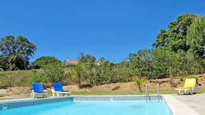 A swimming pool with two lounge chairs, one blue and one yellow, and a clear blue sky.