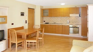 Een kleine keuken met houten kastjes, een eettafel met stoelen en een inbouwoven.