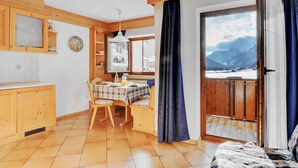Une cuisine chaleureuse avec des meubles en bois, une table à manger dressée pour deux personnes et une vue sur les montagnes par une grande fenêtre.