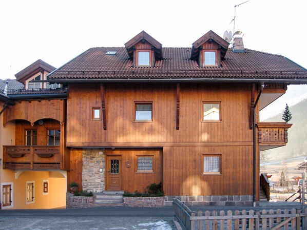 Een houten chalet met een stenen deuropgang, meerdere ramen en een balkon.