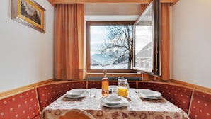 En matplats med ett bord dukat för två personer, ett fönster med utsikt över ett snötäckt landskap och en inramad tavla på väggen.