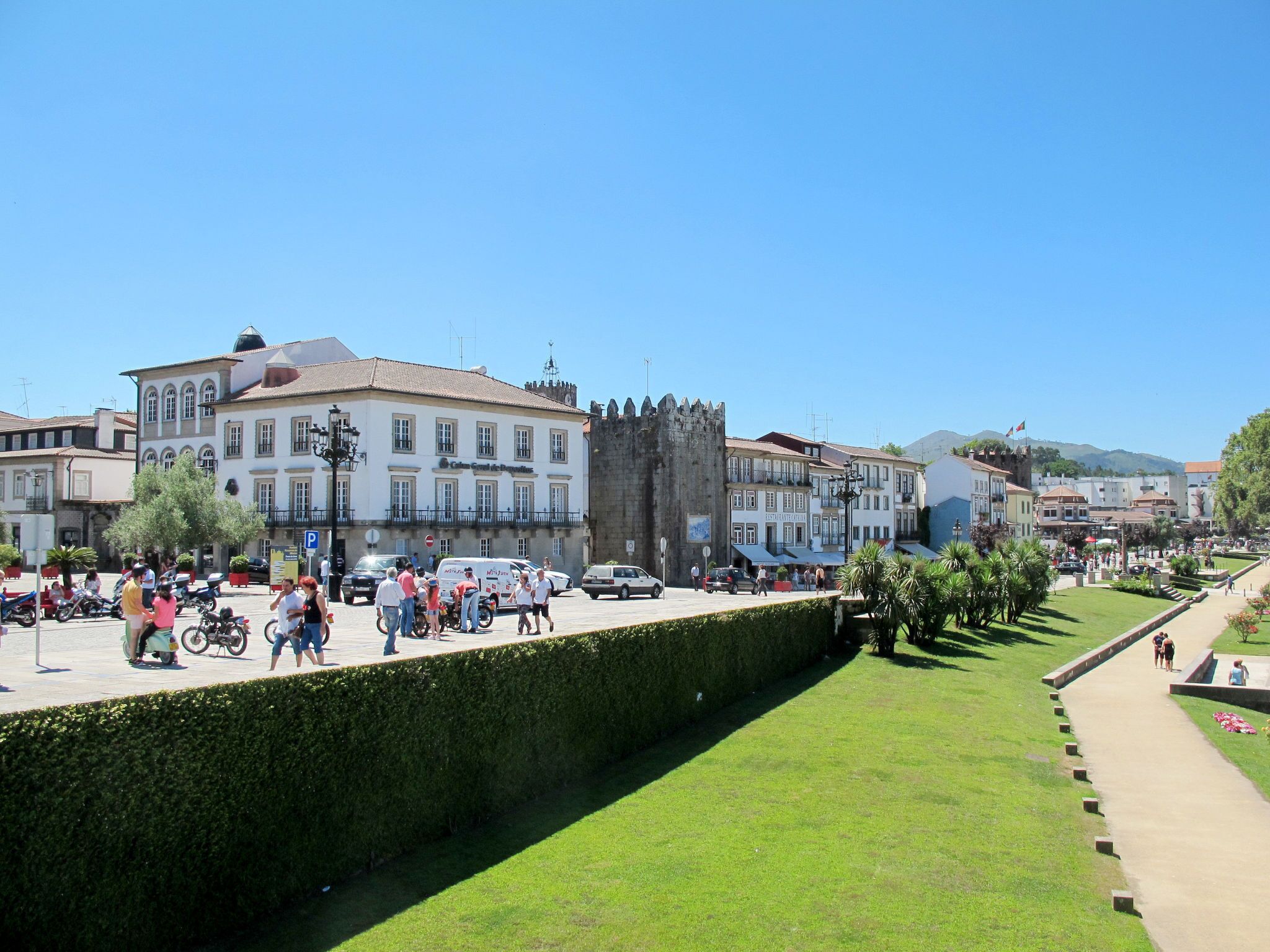 Ein historischer Stadtplatz mit Burg, Kopfsteinpflaster und Fußgängern.