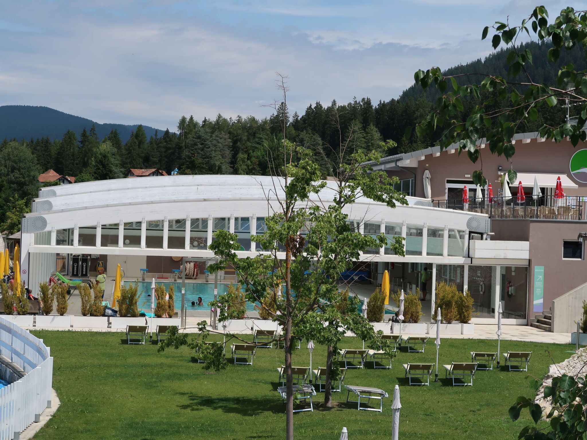 A modern building with a pool area, outdoor seating, and a view of the surrounding forest.