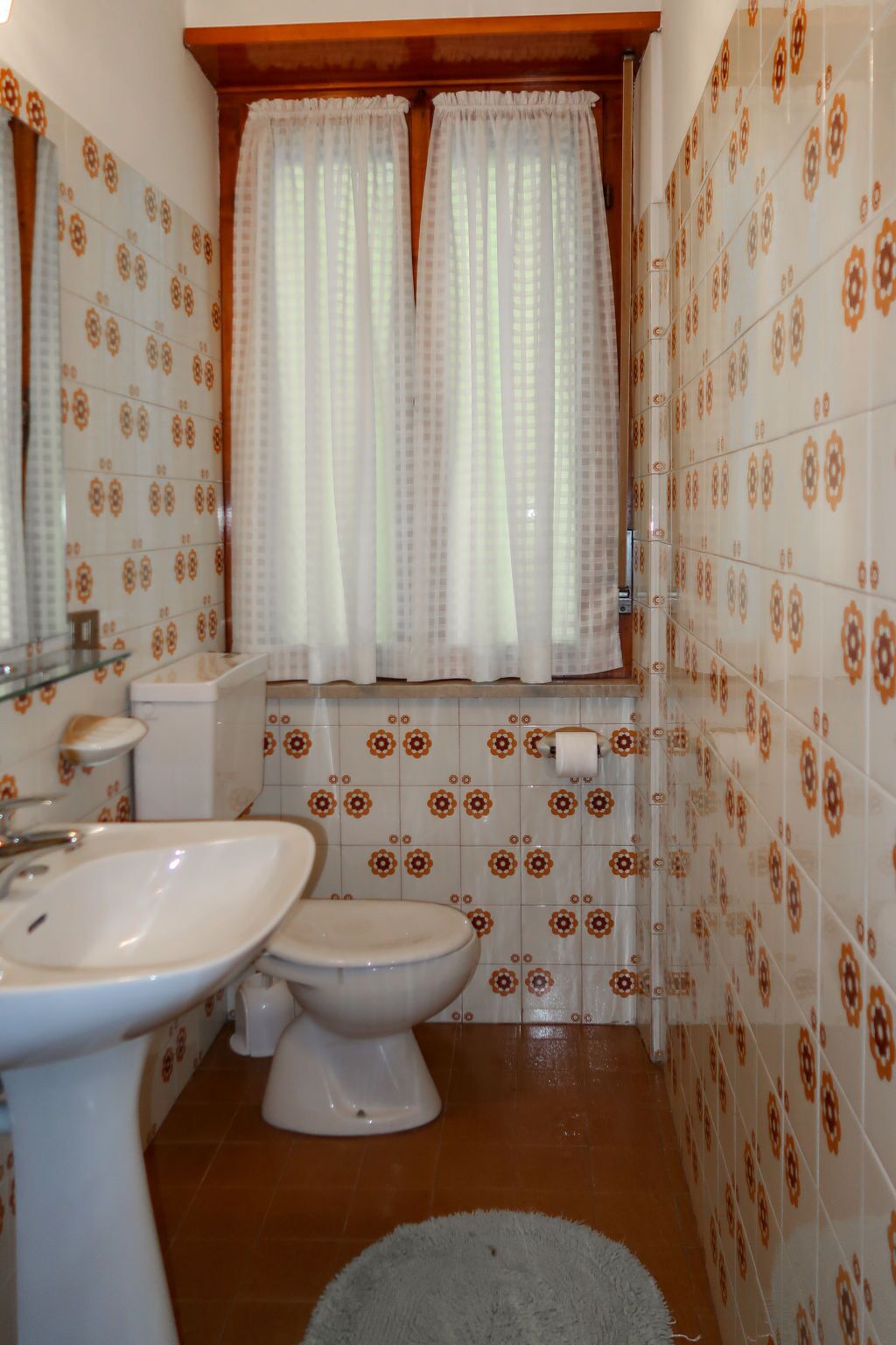 Une salle de bain avec un lavabo, des toilettes et une fenêtre avec des rideaux.