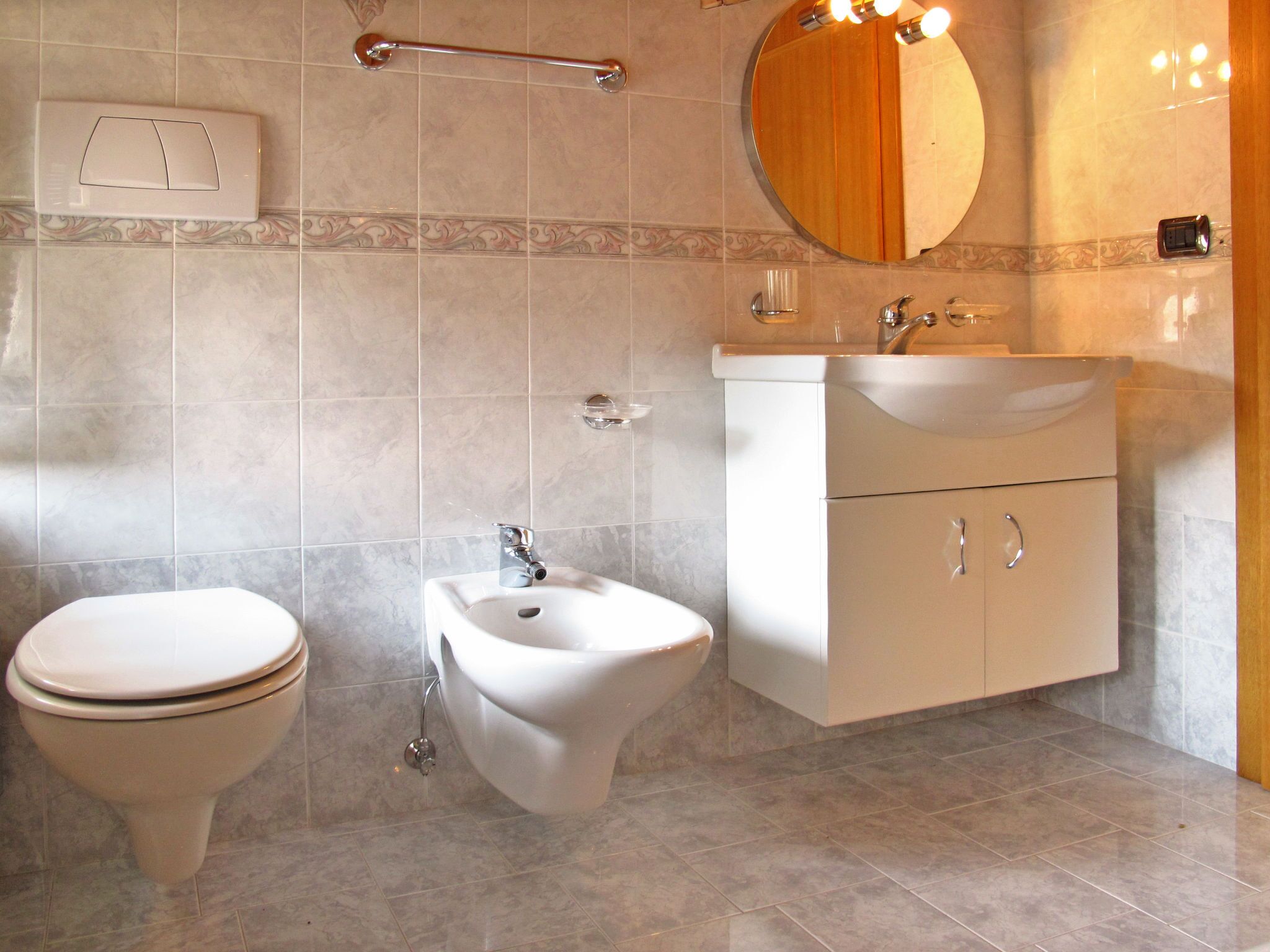 Et moderne badeværelse med toilet, bidet, vaskebord med vask og et spejl.