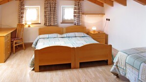 A bedroom with a wooden bed, a desk, a chair, and two windows with curtains. - Giuditta by Interhome (Pozza di Fassa)