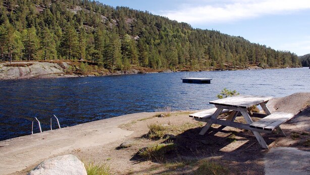 Järvenrantainen piknikalue, jossa on puinen penkki ja betoninen alusta.