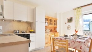 A kitchen with white cabinets, a dining table with chairs, and a window with a view of a snowy landscape.