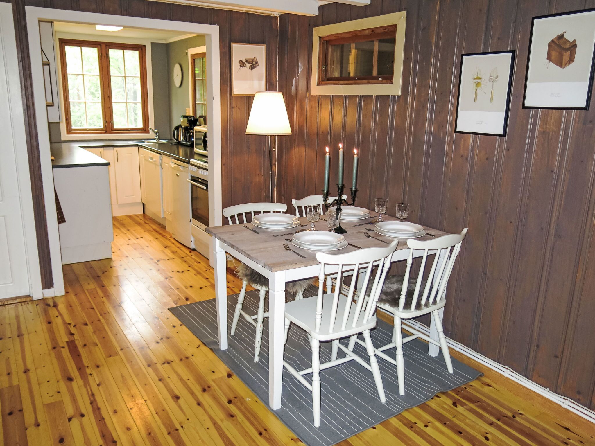 Un coin repas avec une table en bois dressée pour quatre personnes, des chaises blanches et une lampe.