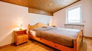 A bedroom with a wooden bed, nightstands, and a window with a view. - Mantina by Interhome (Moena)