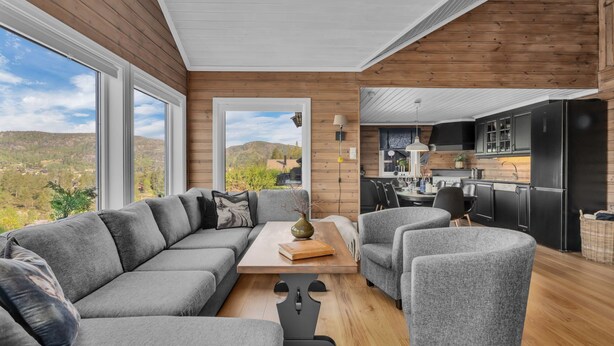 Een moderne woonkamer met een grijze modulaire bank, een houten salontafel en grijze fauteuils.