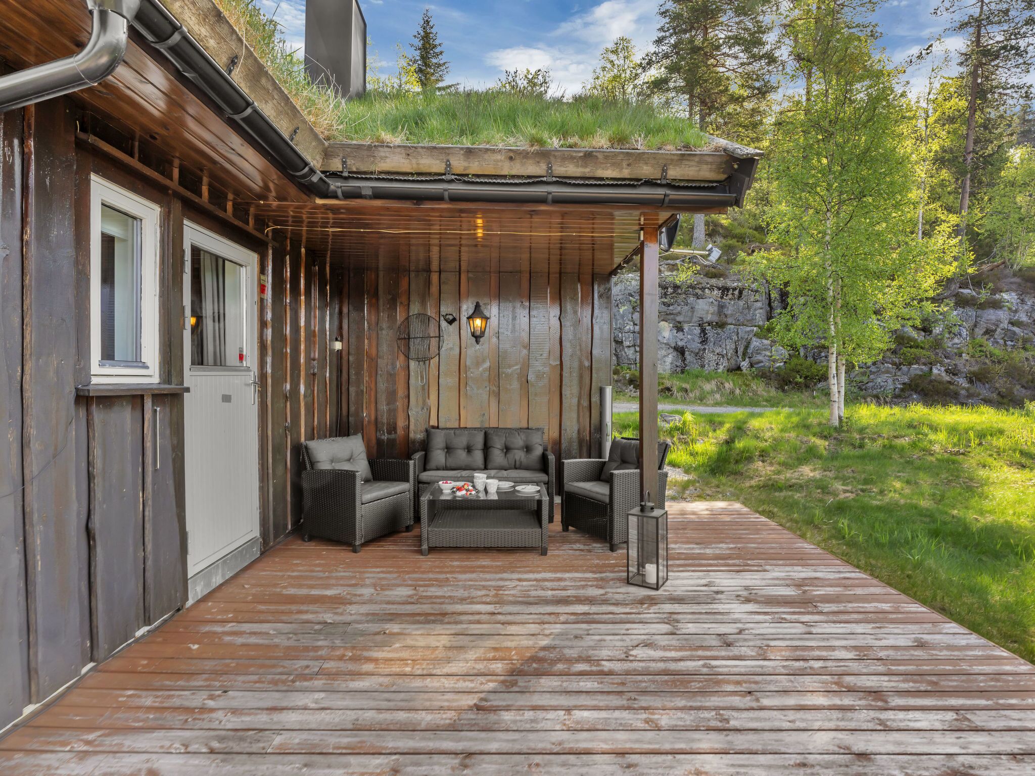 A wooden deck with outdoor seating, a stone wall, and a grassy area.
