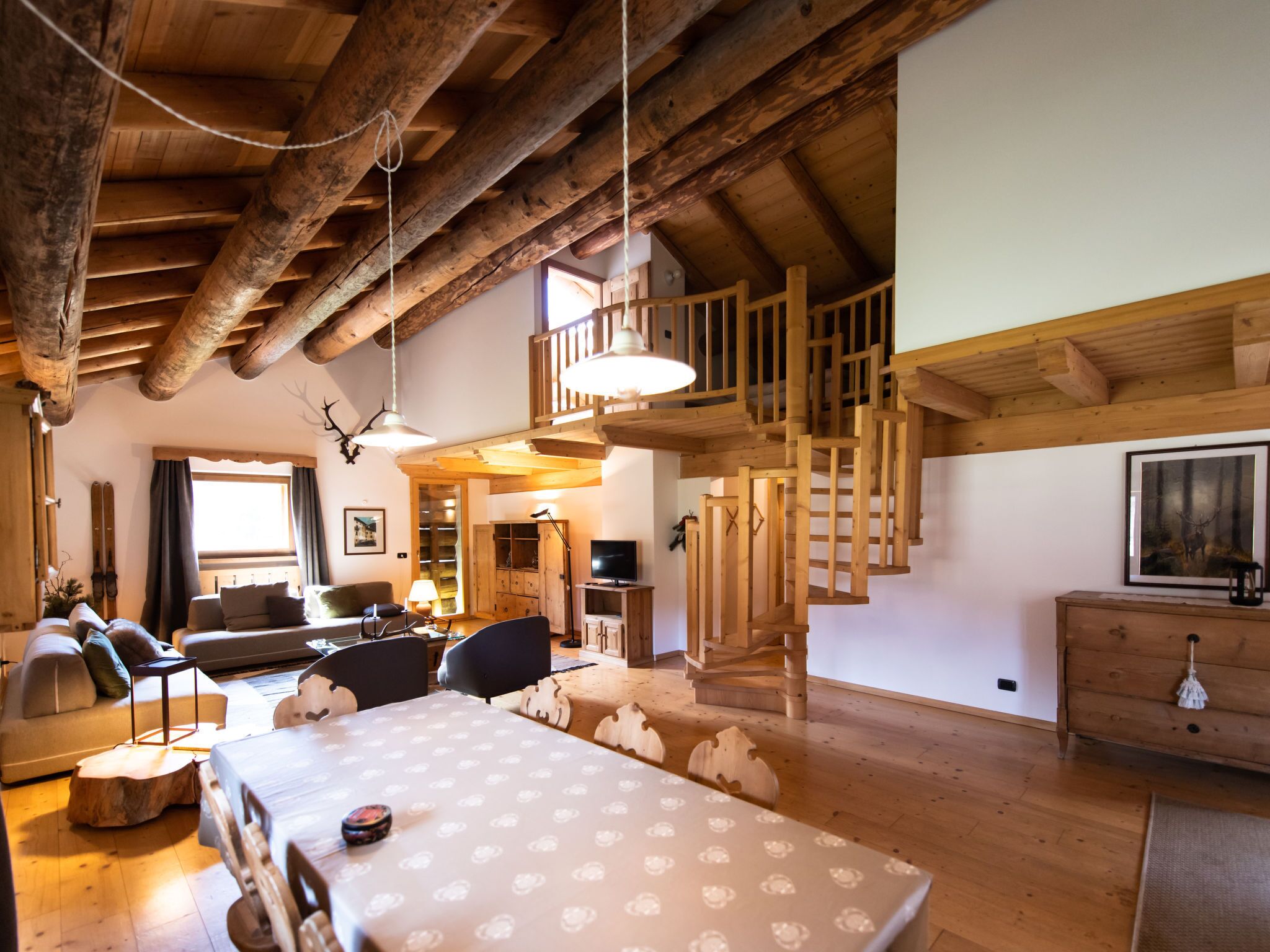 Un amplio salón con techo alto, vigas de madera, una escalera y una mesa de comedor.