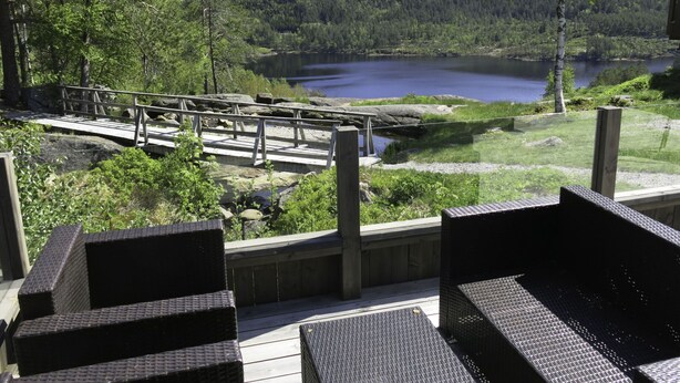 A deck with wicker furniture overlooking a lake and forest.