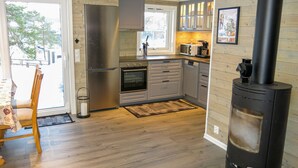 A modern kitchen with a wood stove, stainless steel appliances, and a view to the outside.