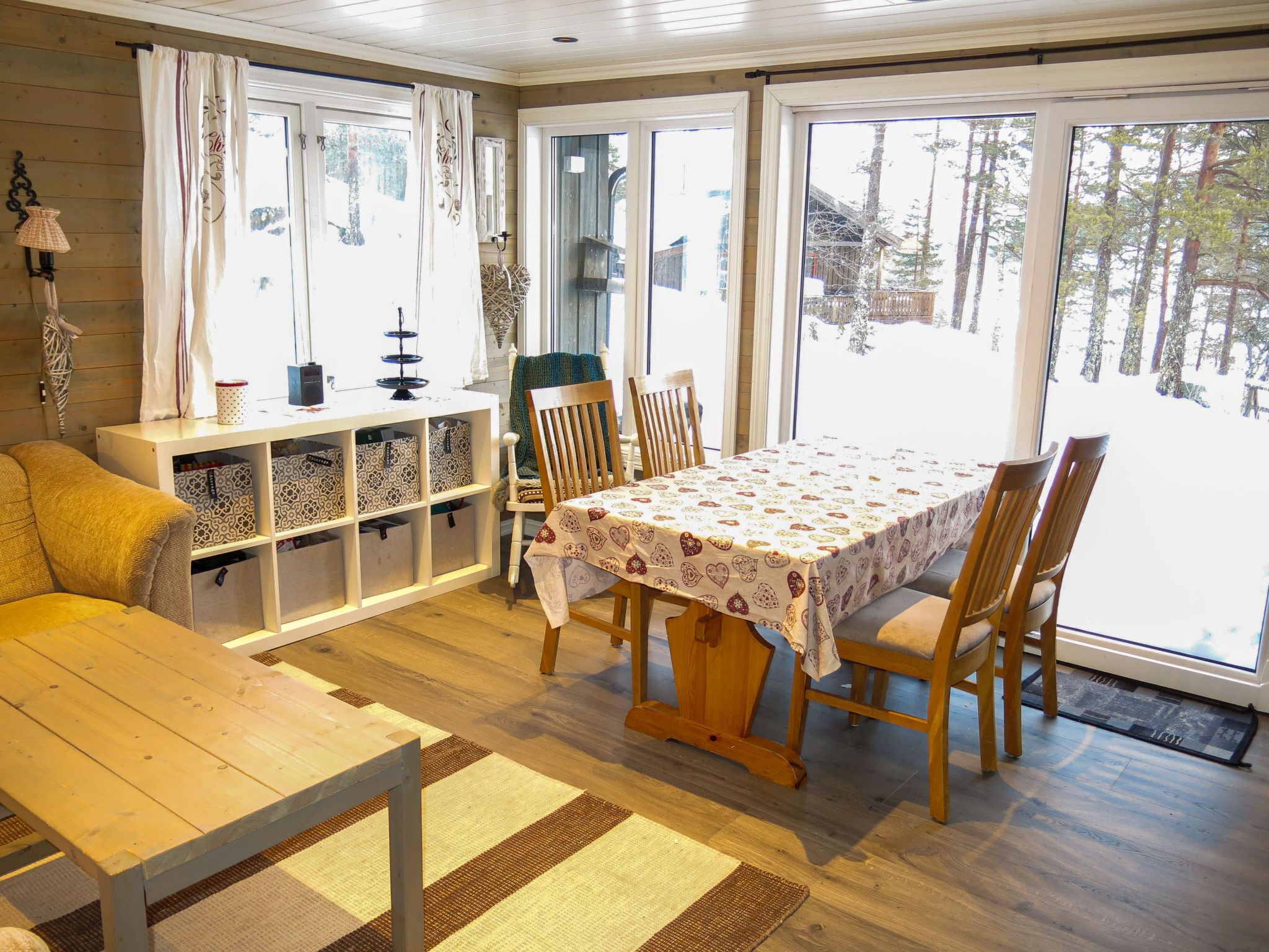 A cozy cabin interior with a wooden dining table, chairs, a bench, and a storage unit with patterned bags.