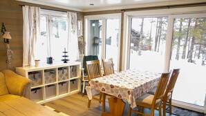 A cozy cabin interior with a wooden dining table, chairs, a bench, and a storage unit with patterned bags.