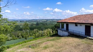 Een wit gebouw met een rood pannendak, een balkon en uitzicht op een groen landschap met velden en bomen.