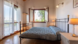 Een slaapkamer met een bed, houten vloer, een raam met uitzicht, een nachtkastje en een lamp.