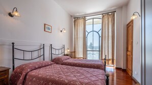 Une chambre avec deux lits, un plancher en bois, une fenêtre avec des rideaux et des lampes fixées au mur.
