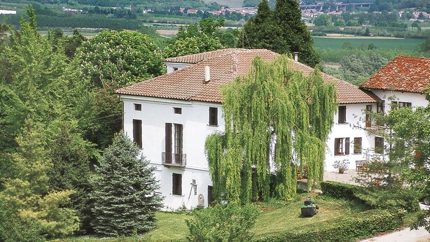 Un bâtiment blanc, doté d’un toit en tuiles, entouré de verdure et d’arbres.