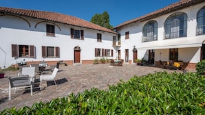 Une cour avec un bâtiment blanc, un sol en pierre et des sièges extérieurs.