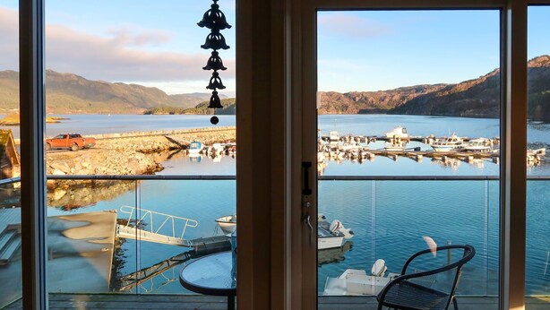 A view from a balcony overlooking a marina with boats, a dock, and a mountainous landscape. - Jektastøo by Interhome (Huglo)