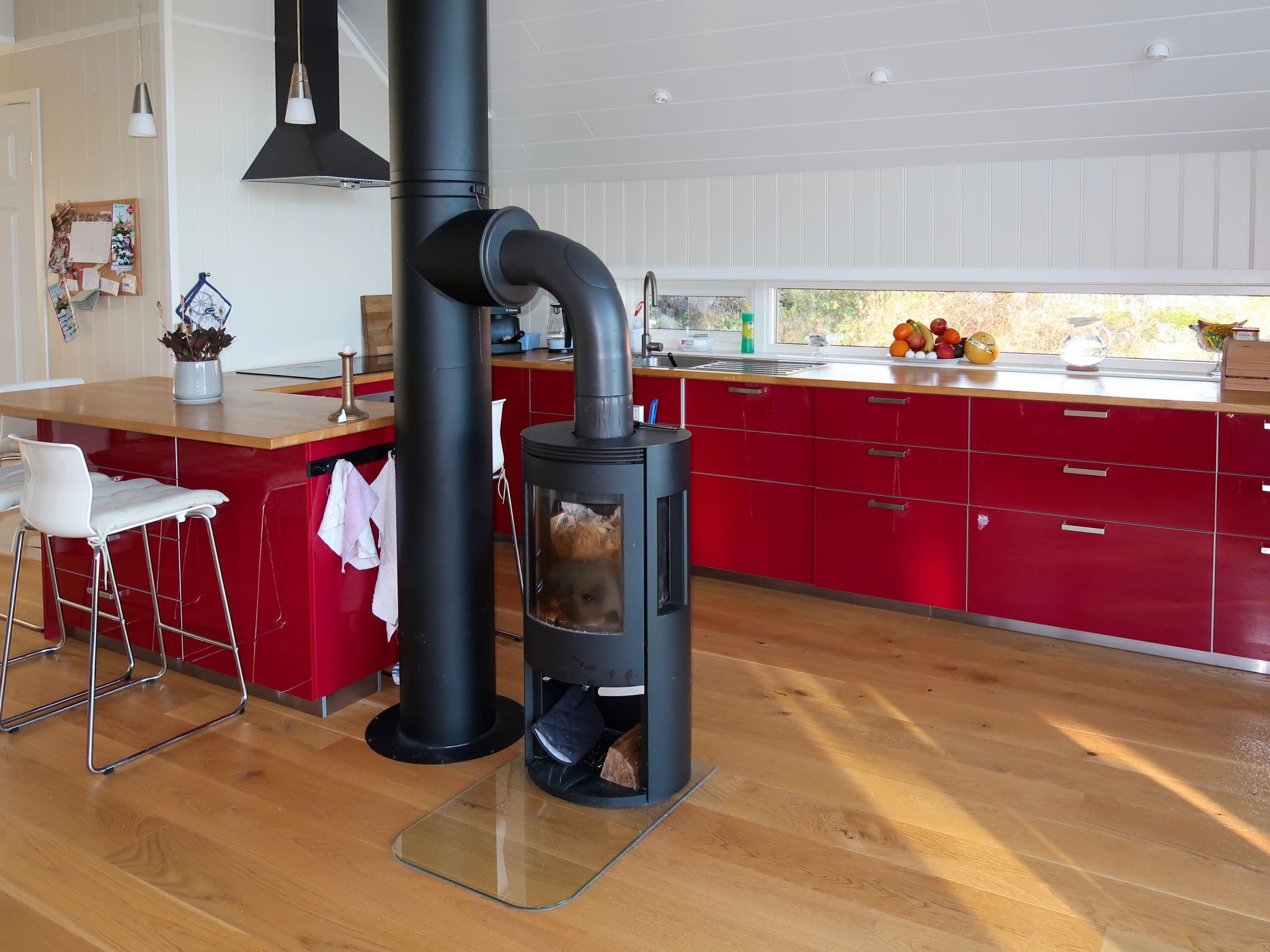 Une cuisine moderne avec un poêle noir central, des armoires rouges et un plan de travail en bois.