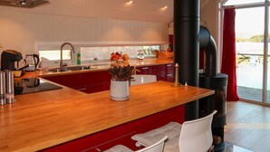 A modern kitchen with a wooden island, red cabinets, white chairs, and a large window with a view of the outdoors. - Jektastøo by Interhome (Huglo)