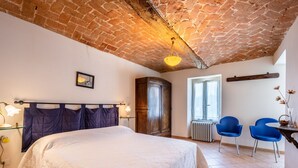 A bedroom with a brick ceiling, a bed with a white duvet, a wooden wardrobe, a desk with two blue chairs, and a window with curtains. - Cascina Villa (AST231) by Interhome (Asti)