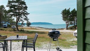 An outdoor patio with a table and chairs, a portable grill, and a scenic view of the sea and mountains. - Nesholmen by Interhome (Leirvik)