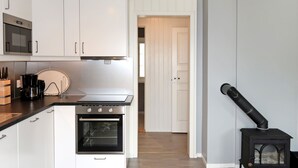 A modern kitchen with white cabinets, a built-in oven, a coffee maker, and a wood-burning stove. - Nesholmen by Interhome (Leirvik)