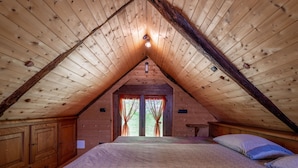 A bedroom with a sloped ceiling, wooden walls, a bed with patterned bedding, and a window with curtains. - Baita Degli Orsi by Interhome (Domodossola)
