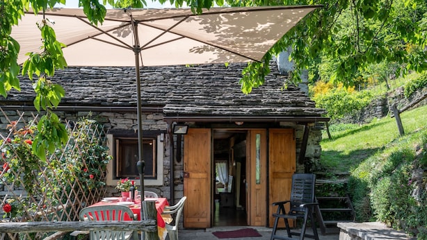 A stone building with a wooden door and a table with chairs outside. - Baita Degli Orsi by Interhome (Domodossola)