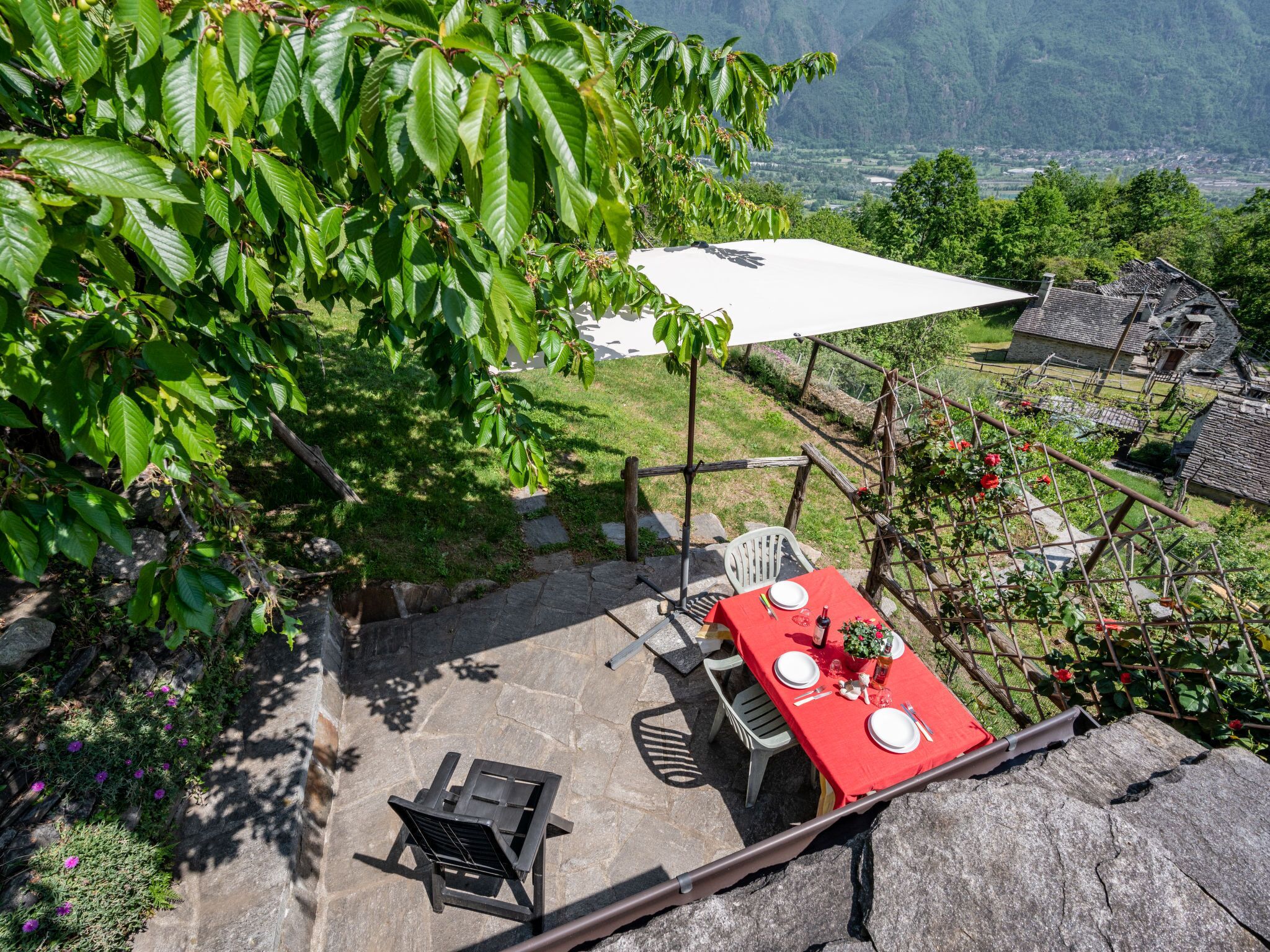 Une terrasse avec une table et des chaises, entourée d’une végétation luxuriante et offrant une vue sur une vallée.